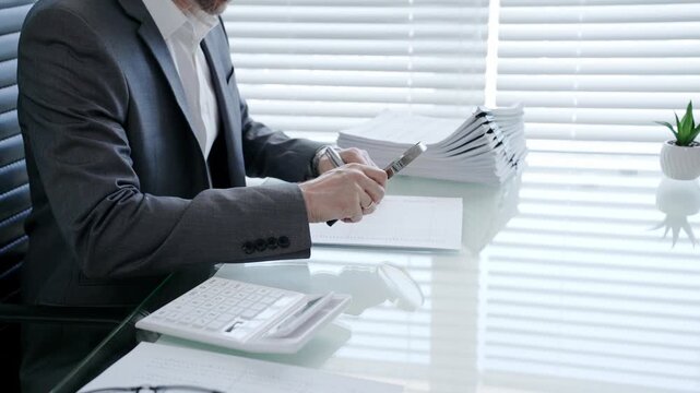 Businessman using a magnifying glass to meticulously examine a financial document at a modern office desk, scrutinizing details for accuracy and compliance in auditing processes