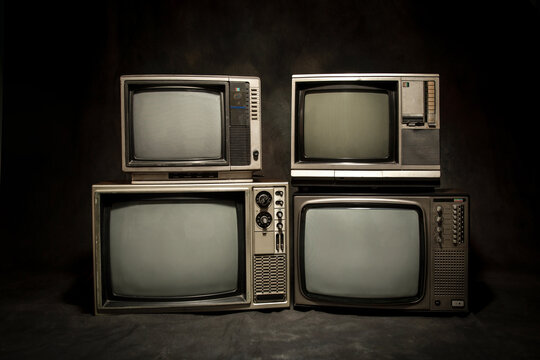 Four retro style, old television sets stacked with blank screen against a dark background.