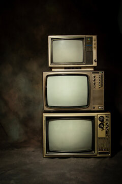Three retro old televisions pile with blank screen on a dark background