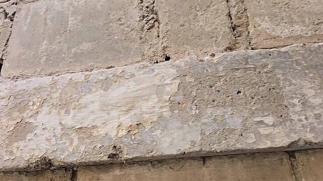 Close-up video of a rustic concrete block wall with weathered, flaking plaster and worn cement surface showing raw, unfinished architectural construction texture.