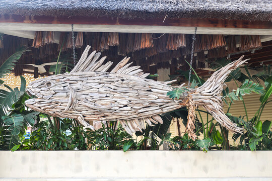 Large decorative fish sculpture crafted from wooden branches and pieces creative outdoor art installation in natural setting.