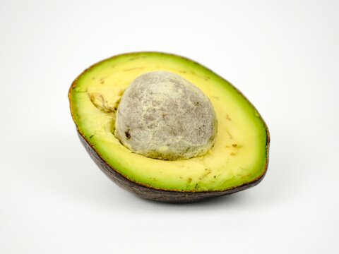 Single half of a ripe fresh avocado with a large central seed, showing soft creamy green flesh, isolated on a clean white background