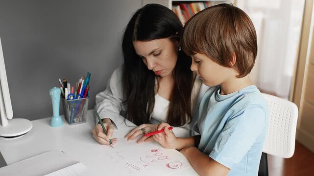 4K slow motion 60fps footage of a caring caucasian mother helping her young son drawing pictures with colorful pencils on paper at a white desk indoors.
