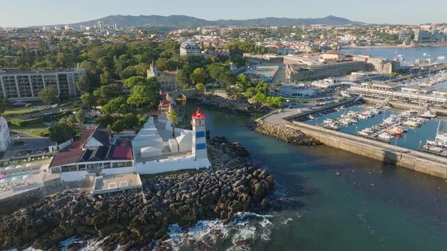 Aerial view of Santa Marta lighthouse and Cascais marina with moored yacht boats with Cascais cityscape, Portugal on sunset. Orbit parallax shot