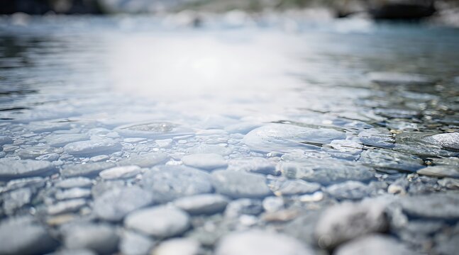 Sunlight creates bright reflections on the surface of calm, clear water over a bed of smooth river stones.