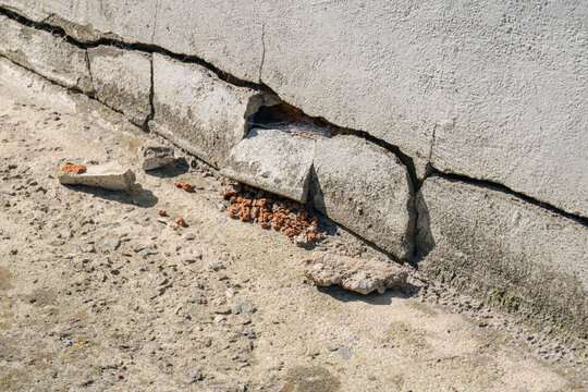 Crack in concrete wall and damaged house foundation base, close-up view of structural damage and construction defect, building repair, maintenance and restoration concept
