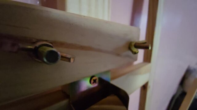 A close-up shot focusing on a threaded metal bolt and wing nut fastening wooden parts of an artist easel structure.   