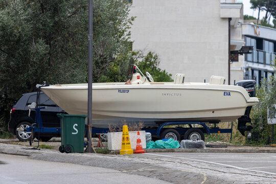 June 30, 2026: Sveti Stefan, Montenegro, White small motorboat sits on trailer next to parked cars on residential street, with traffic cones, plastic rubbish bags, and recycling bin along curb under o
