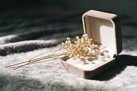 Open cream velvet lined jewelry box with a gold earring and dried flowers on a white blanket