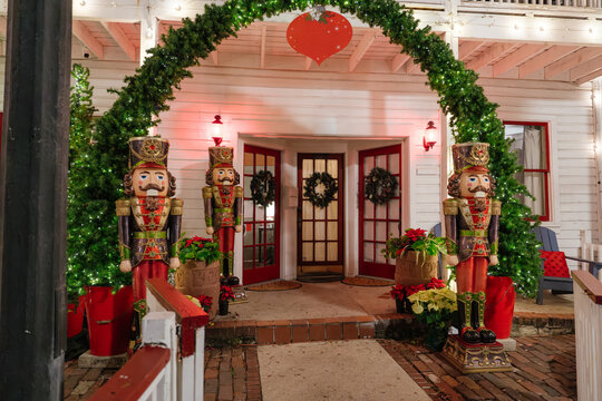 Three giant nutcracker soldiers stand beneath an illuminated garland arch in St. Augustine, Florida. Christmas trees, wreaths, poinsettias, and red ornaments decorate the historic building entrance.