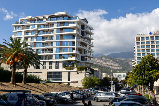 September, 17, 2026, Budva, Montenegro, Street-level view of modern midrise apartment buildings beside coastal road, with parked cars and palm landscaping, sunlit facades reflecting blue sky, and dist
