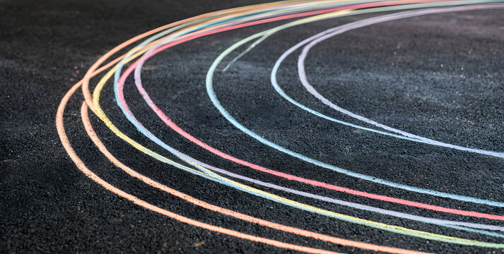 Vibrant chalk markings stretch across the dark asphalt. An abstract design with soft colors contrasts with the rugged surface, offering a whimsical setting for artistic endeavors and visual compositio