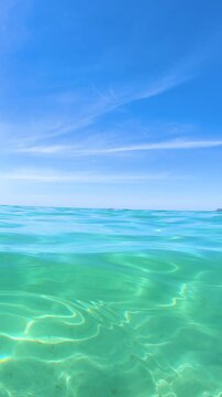 Vertical slow motion view of turquoise Mediterranean sea beneath a clear blue sky in Sardinia, Italy, creating a peaceful scenic coastal background.