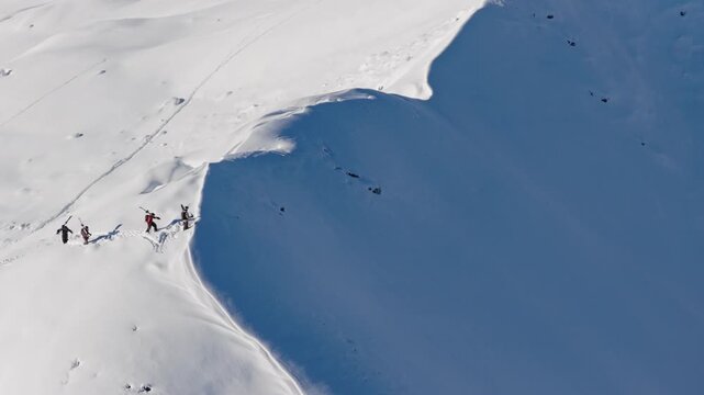 Aerial footage of four ski mountaineers carrying skis on their backs while climbing a snowy mountain ridge. Winter adventure in the Austrian Alps captured in cinematic 4K detail.