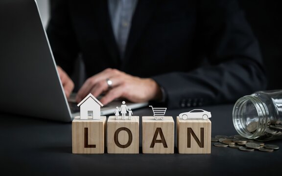 Business loan concept with wooden blocks spelling loan, icons of house, family, shopping cart, and car, with a laptop and coins