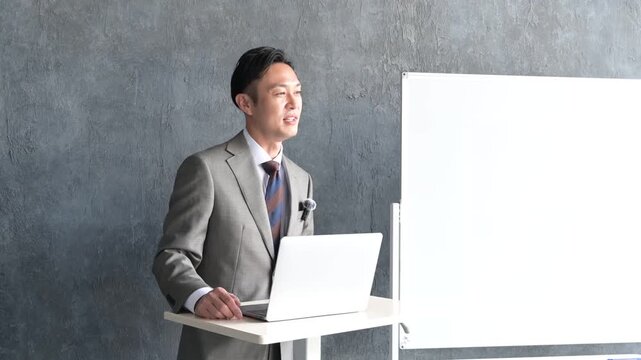 グレー背景でプレゼンをするスーツを着た日本人男性