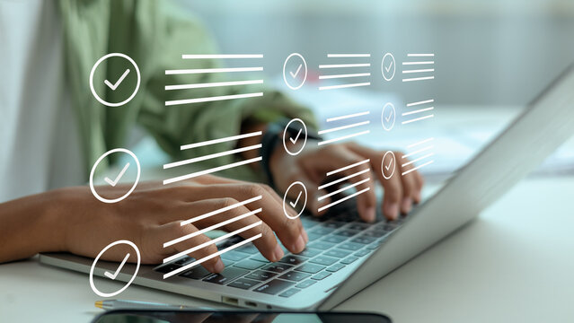 Close up of businessman working on laptop keyboard to complete online survey, managing digital task checklist form with virtual checkmark icon graphics in office.