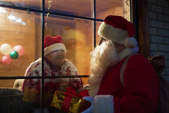Cute boy  looking out the window. Authentic Santa Claus standing outside the window with a gift.