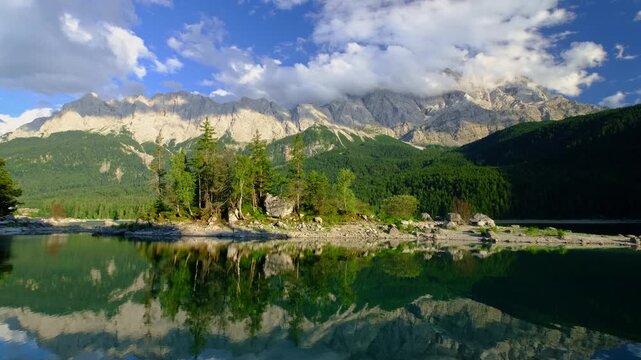 Static view of a pine-covered island in Eibsee lake with the Zugspitze mountain range and clouds in the Bavarian Alps, Germany