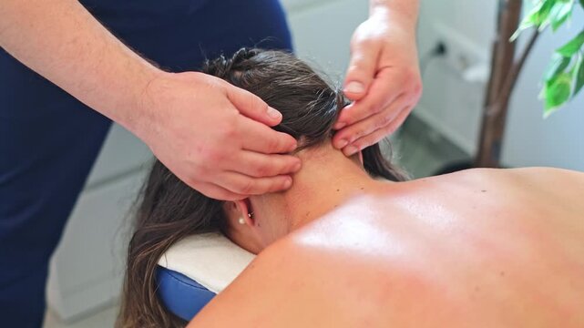 A male massage therapist works on a female client's neck and back with manual massage techniques in a personal care studio