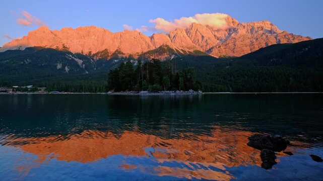 Static view of Zugspitze mountain peaks glowing with orange alpenglow at sunset over Eibsee lake in Bavaria, Germany