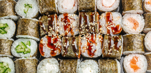 Assorted sushi rolls arranged in rows with rice, seaweed, cucumber, salmon, sesame seeds, and colorful fillings viewed from above on a serving platter © Надія Коваль