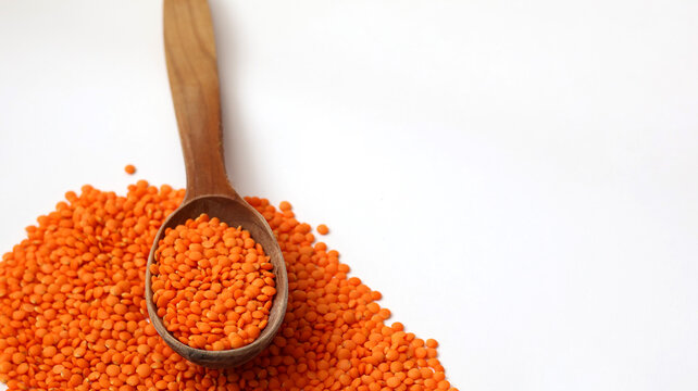 Red lentils in wooden spoon with copy space. Organic raw orange legume grains isolated on white background.