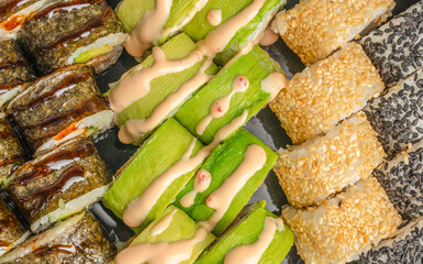 Assorted sushi rolls with avocado, cucumber, sesame coated rice, seaweed wrapped fillings, creamy sauce and pink garnish arranged on a platter, Japanese cuisine closeup © Надія Коваль