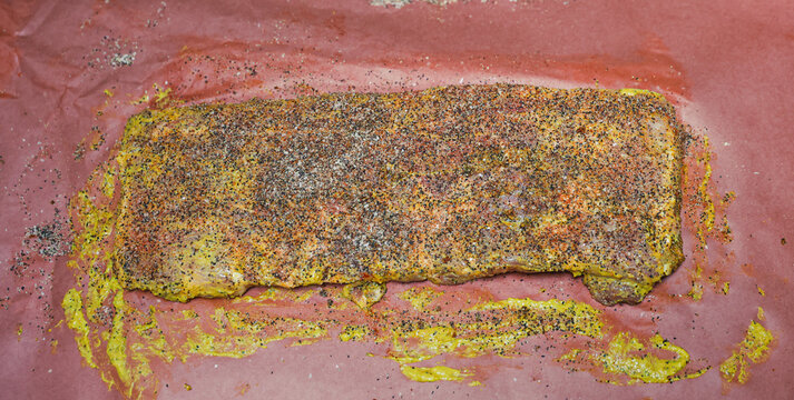 Barbecue pork ribs smothered in mustard, black pepper, salt, and garlic powder resting on butcher paper before going in the pellet grill smoker to cook.
