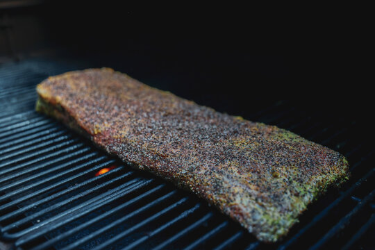 Barbecue pork ribs seasoned with salt, pepper, garlic for a crunchy bark. The bbq meat is cooking on a pellet grill smoker. 