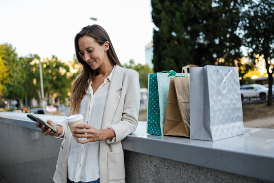 Woman checking phone after shopping with coffee