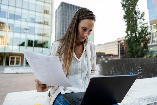 Professional woman working outdoors reviewing documents and laptop