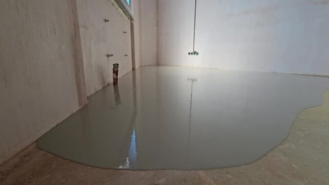 Close-up shot of self-leveling floor compound poured onto a surface and spreading out evenly. Construction worker leveling the floor. Liquid screed flows and fills the surface. Renovation and construc