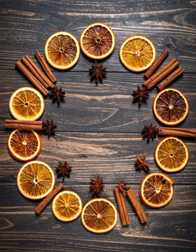 Dried orange slice and cinnamon stick circle on rustic wooden table with star anise, seasonal food arrangement creating warm festive mood