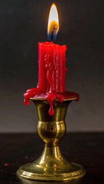 Red candle flame on ornate brass candlestick against dark background, creating warm dramatic still life with dripping wax and reflective metal detail