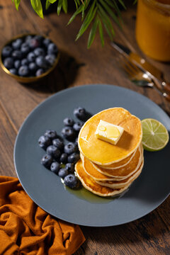 Golden Pancake Stack with Blueberries, Butter and Syrup on Rustic Table
