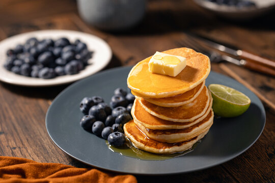 Golden Pancake Stack with Blueberries, Butter and Syrup on Rustic Table