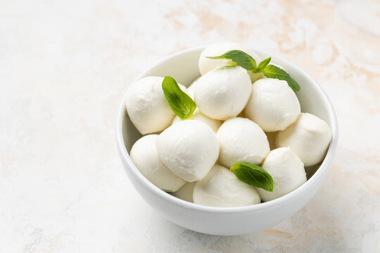 Fresh mozzarella cheese balls arranged in a white bowl with a clean minimalist composition and neutral background.