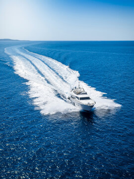 Aerial view of an luxury yacht cruising over the ocean leaving a trail of white surf and waves