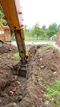 Yellow excavator digs a narrow trench in the soil, groundwork excavation, heavy equipment site.