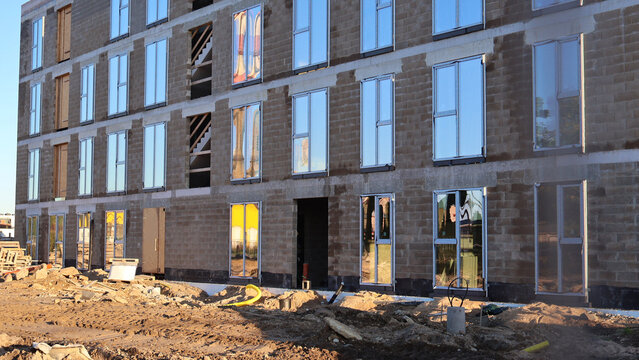 Unfinished apartment building facade with recently installed windows reflecting the sunny sky and surrounding environment, indicating ongoing construction and urban development for new housing