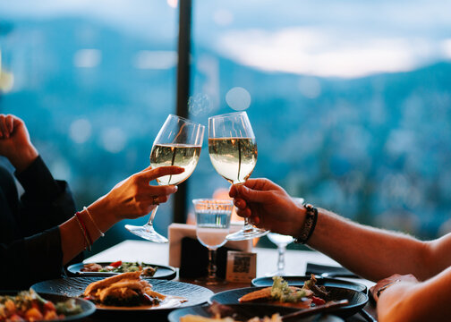 Couple clinking wine glasses at a restaurant table during sunset with a scenic mountain view
