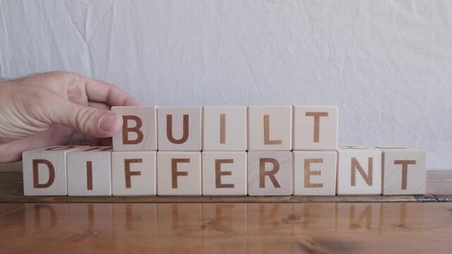 motivational word Built different, laying out by hand from letters on wooden cubes, slow motion
