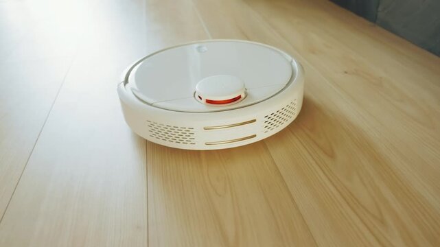 close-up white robot vacuum cleaner while cleaning removing dirt dust in home room wooden floor apartment. robotic vacuum moving working at modern interior laminate flooring, parquet, ceramic tiles