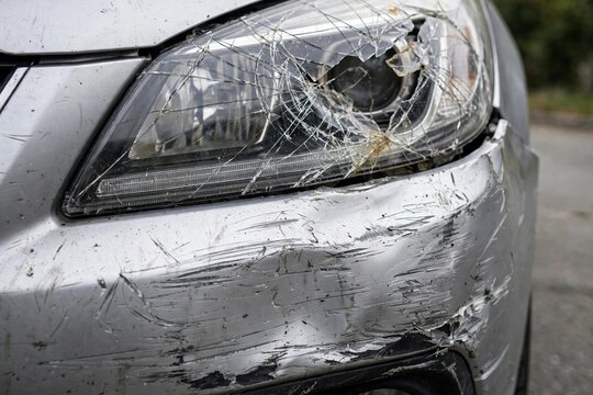 Close Up Of Silver Car Broken Headlight And Scratched Bumper After Front Collision Accident For Insurance Claim