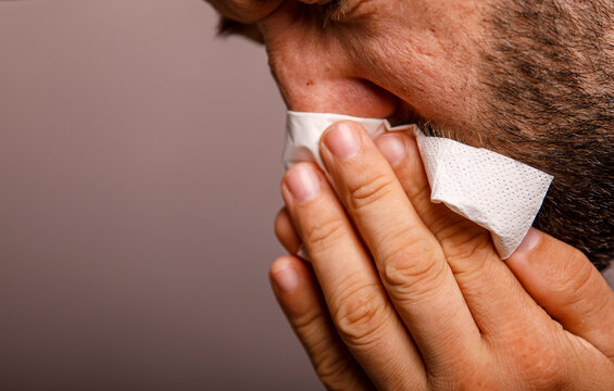 Close-up of a man's hand holding a tissue to his nose, suggesting cold, allergy, or hygiene.