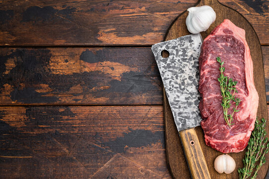 Fresh New York strip steak with thyme and metal cleaver on textured wooden board ideal for barbecue recipe and grill menu designs.