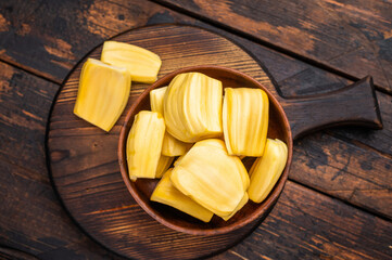 Sweet, golden jackfruit pods (bulbs) in a wooden bowl on a rustic dark wood table. Tropical fruit snack with copy space. © Mironov