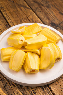 Sweet, golden yellow jackfruit pods (bulbs) served on a white plate on a rustic wooden table. Fresh, tropical fruit snack.