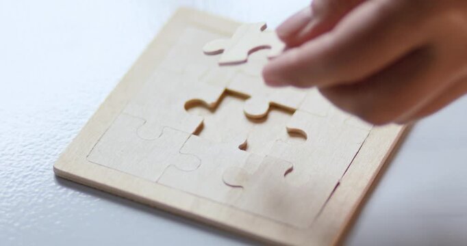 Hand placing a wooden jigsaw puzzle piece on a board, problem solving, solutions, strategy, logical thinking, concentration and completion